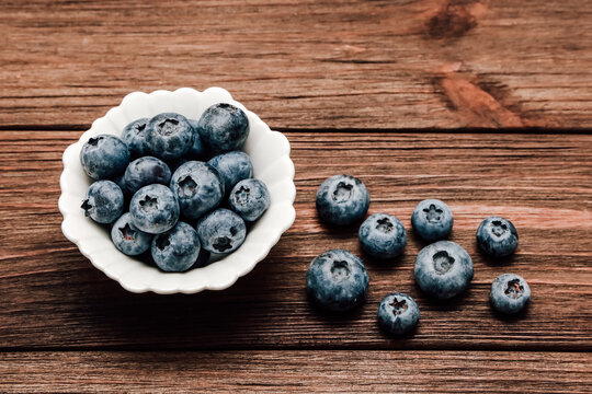 Fresh blueberries in a bowl on a wooden table with some berries scattered around