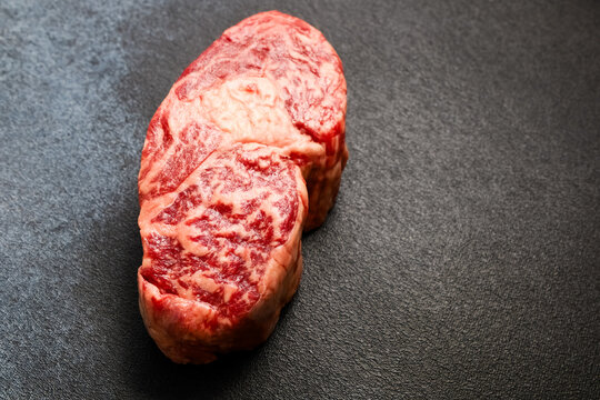 Fresh cut of raw marbled beef resting on a dark surface in a kitchen setting