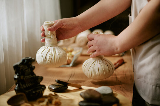 Hands of female therapist holding herbal compress balls for traditional massage treatment. Image suitable for wellness center marketing and spa service promotion, close up shot