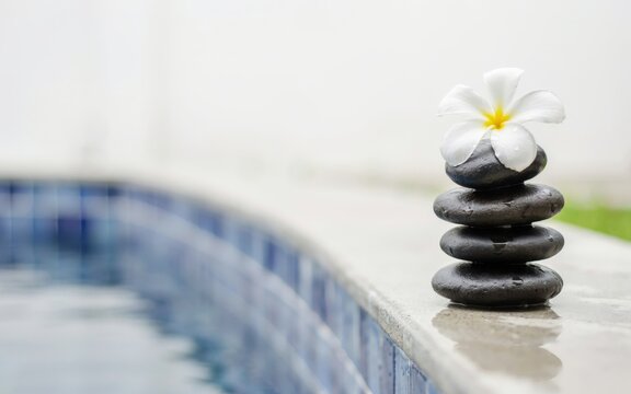 Stack of spa stones with a white frangipani flower by a swimming pool