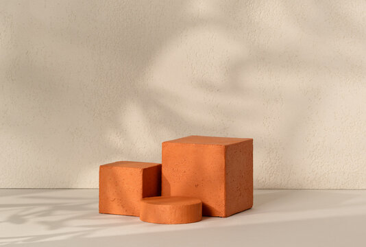 A terracotta textured cube podium paired with a small cylinder pedestal centered on a white surface against a textured beige wall background, offering geometric product display scene
