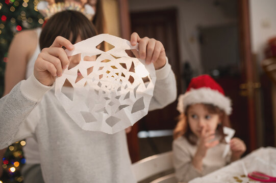 Happy family cut paper snowflakes near Christmas tree, celebrating Christmas with together. New Year's preparations and decorations. Paper crafts. 
