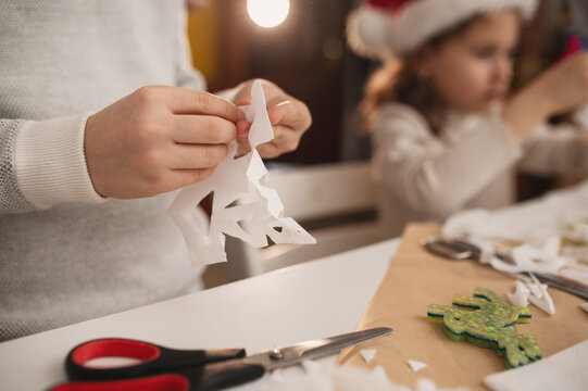 Happy family cut paper snowflakes near Christmas tree, celebrating Christmas with together. New Year's preparations and decorations. Paper crafts. hands closeup