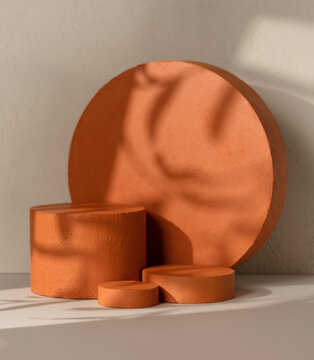 Three terracotta textured cylinder product display podiums  arranged in front of a large terracotta round disc on a beige wall background with leaf shadow overlay.