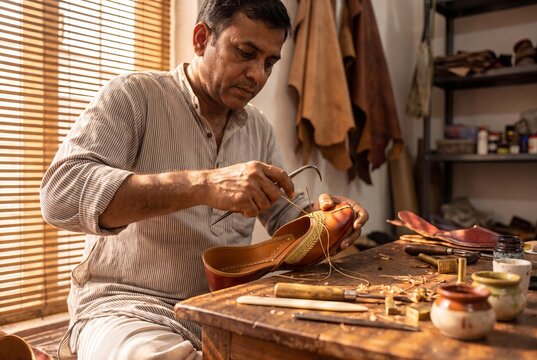 Artisan hand stitching traditional leather jutti shoe with awl in workshop