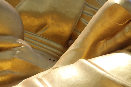 Abstract close-up of golden Buddha statue drapery with birds