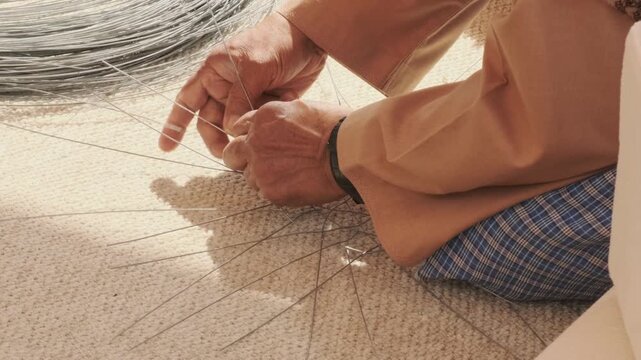 elderly man hands weave metal wire to create fish trap. ghazl al gargour shows authentic arabic craft. ghazl al gargour preserves ancestral skills passed through generations.