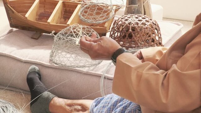 elderly man unwinds metal wire preparing to weave fish trap near finished cages. ghazl al gargour shows authentic arabic craft. ghazl al gargour passes mastery down through generations.