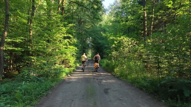 Two friends riding bicycles on dirt path through summer forest