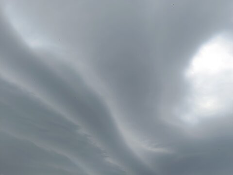 Sweeping bands of grey clouds in an overcast sky. Dramatic stormy weather background. Sun obscured by thick cloud cover