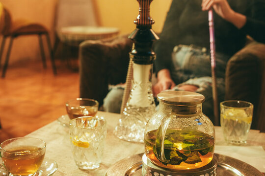 Girl smoking hookah while drink green tea with fresh mint inside narghile' bar - Young people lifestyle concept - UGC flash content - Main focus on teapot