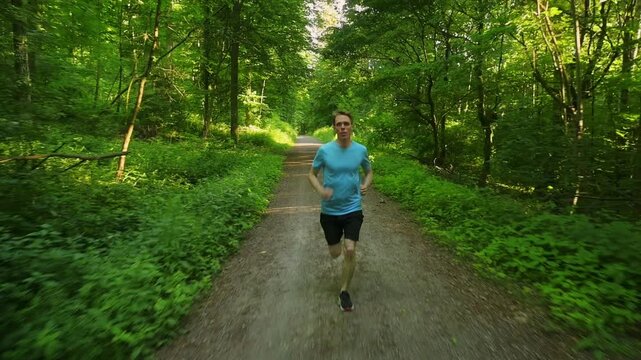 Young man running in a green forest on a dirt road. Slow motion sports action shot with an athlete in nature.