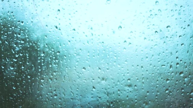 Raindrops cover the glass, creating a blurred view of the outside. The rain impacts the atmosphere, lending a calm feel to the scene.