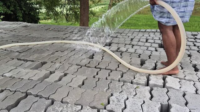 Worker Spraying Water On Interlocking Concrete Paver Blocks For Curing Close Up