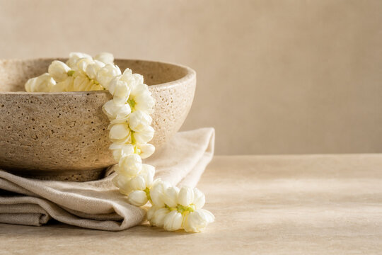 Sampaguita garland draped over travertine bowl with linen napkin, still life concept