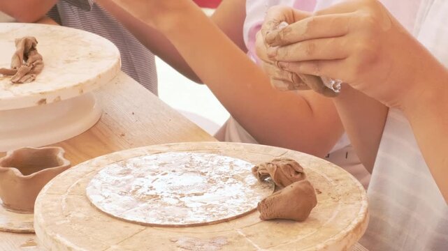 child hands shape wet clay on potter's wheel during pottery workshop. child learns traditional craft. child develops creativity and motor skills with potter's wheel.