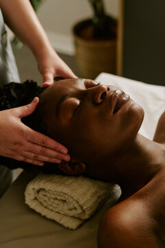 Vertical image of young adult African American woman receiving relaxing head massage from therapist. Perfect for wellness center advertising and beauty salon marketing campaigns