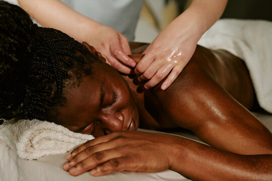 Young adult African American woman receiving back massage from therapist in wellness center, promoting self care and body treatment. Close up shot