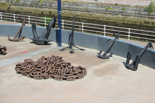 Row of ship anchors and a coil of heavy chain in front of an old stone dock wall