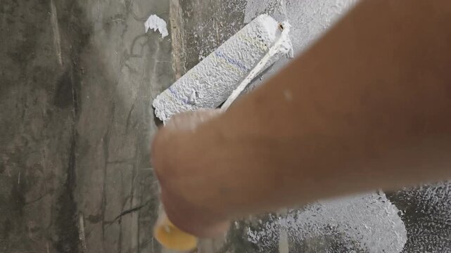 a paint roller applying white paint along the inner corner seam of a raw concrete wall, ideal for home renovation, edge painting, DIY repair, wall priming, and interior construction concepts.