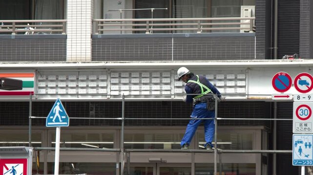 Japanese Construction Worker on Scaffolding During Urban Building Renovation