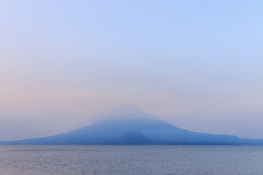 Misty blue volcano rising above a calm sea