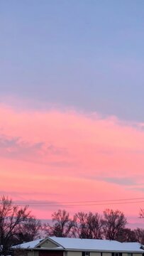 Beautiful pink sunset sky over a snowy house roof.