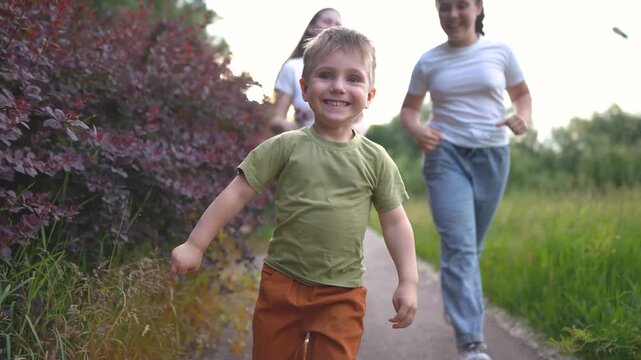 A boy joyfully runs along a path, while two girls run behind him. The boy's laughter echoes as they race through the lush greenery of the park.