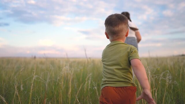 A boy in a green shirt and brown shorts runs through tall grass, as a girl in a white shirt leads the way. The boy and girl play in the open field.
