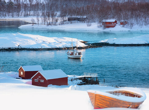 Fisher shelter with fishboat at sunset in the background snowy mountains and Norwegian fjords in winter - Tromso, Norway