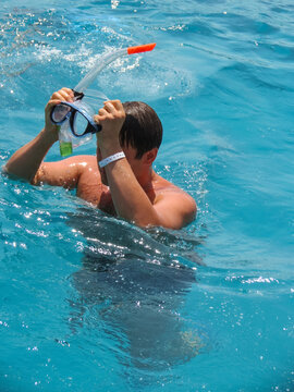 Young male snorkeler adjusts mask and snorkel while swimming in clear turquoise water, sunlight reflecting on the surface creating a vibrant aquatic scene. Egypt, Hurghada