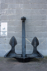 Naklejka premium Bilbao, Spain - August 12, 2026: A large ship anchor against a grey marble wall on a paved quay