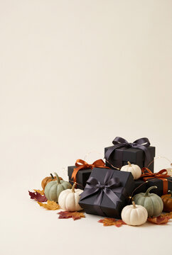 Black gift boxes with bows and decorative pumpkins on autumn leaves