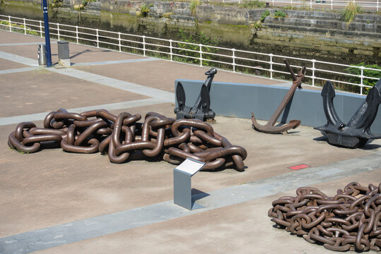 Coils of heavy anchor chain and ship anchors on a paved quay beside a dry dock