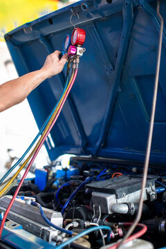 Auto mechanic using a manifold gauge set to check pressure and recharge Freon in a car air conditioning system under the open hood in a garage workshop.
