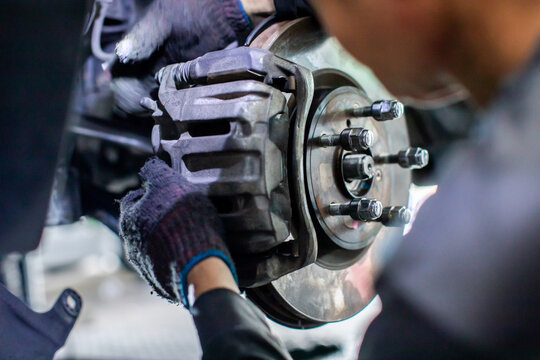 Selective focus to Professional mechanic wearing protective gloves repairing and inspecting a car disc brake caliper and rotor system in an auto service garage workshop.