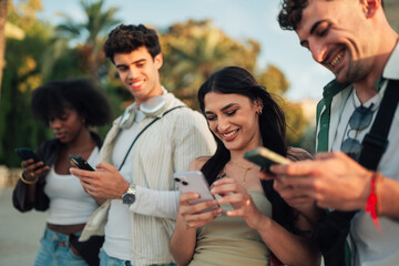 Obraz premium Young friends connecting with smartphones outside, enjoying social media and technology addiction culture