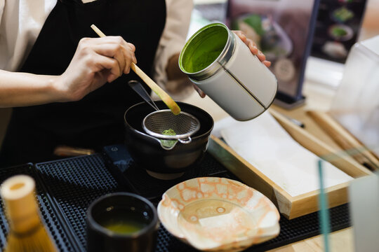 Barista sifting green matcha powder on strainer to prepare Japanese green tea.