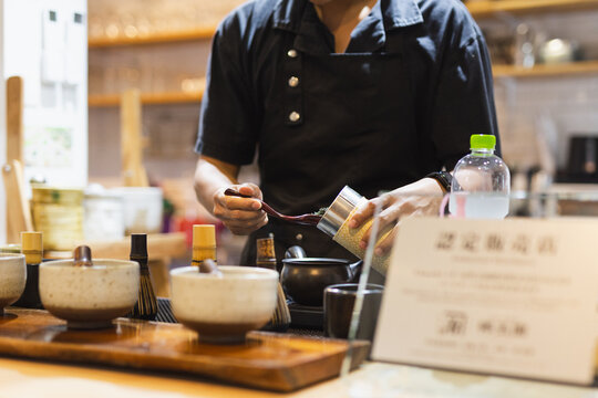 Barista in uniform scooping tea leaves into a teapot in modern counter.