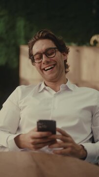 Vertical portrait of young man in glasses and white shirt sitting in office using smartphone. Expression changes from happy and smiling to confused and frustrated, to awkward and sheepish.