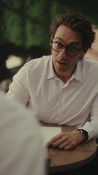 Young male student with glasses feeling stressed while taking difficult college exam, secretly asking friend sitting opposite for answers, illustrating academic dishonesty and cheating, slow motion.