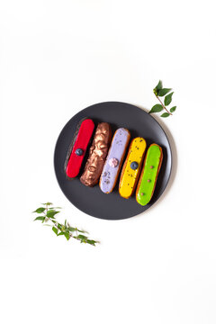 Colorful gourmet eclairs with glazed topping on plate - modern pastry flat lay in soft natural light, top view dessert concept