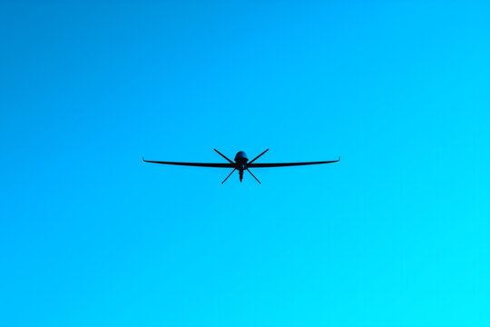 Silhouette of Military Drone Flying Against Blue Sky