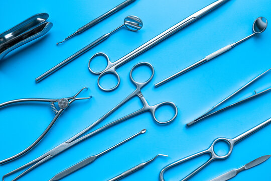 Pattern flat lay of stainless surgical instruments and tools on blue table, top view. Medical background