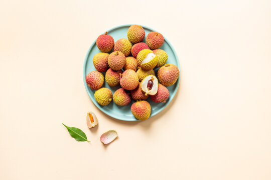 Fresh lychee fruit with green leaves on a plate, top view