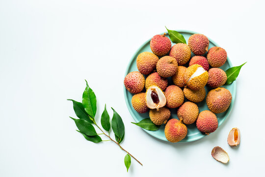 Fresh lychee fruit with green leaves on a plate, top view