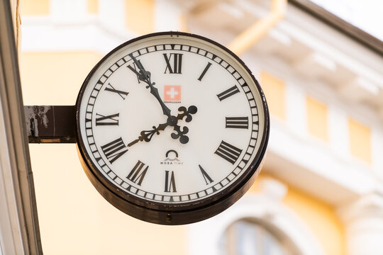 Vintage street clock with Roman numerals mounted on a historic building facade. Timekeeping, urban architecture, city landmark