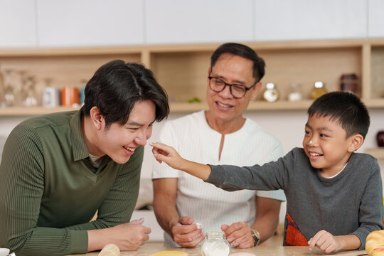 Asian grandfather father and son playing with flour while baking in kitchen for family bonding