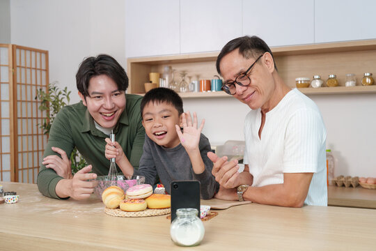 Multigenerational Asian family on video call with smartphone while baking in kitchen