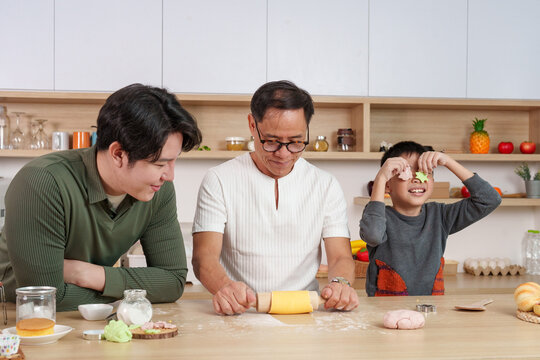 Playful Asian boy holding cookie cutters to eyes while baking with family